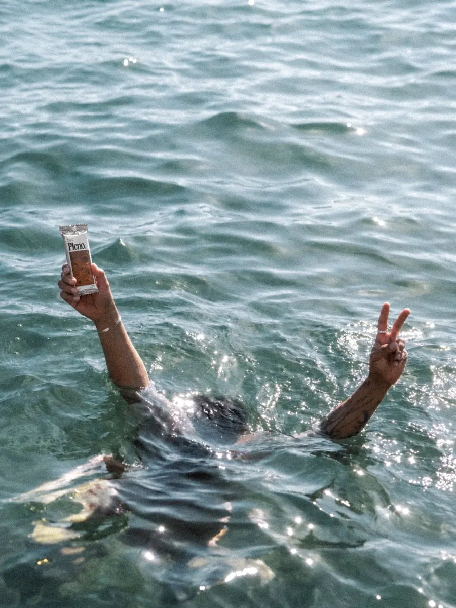 Swimmer holding a Goldie chocolate bar above sunlit water